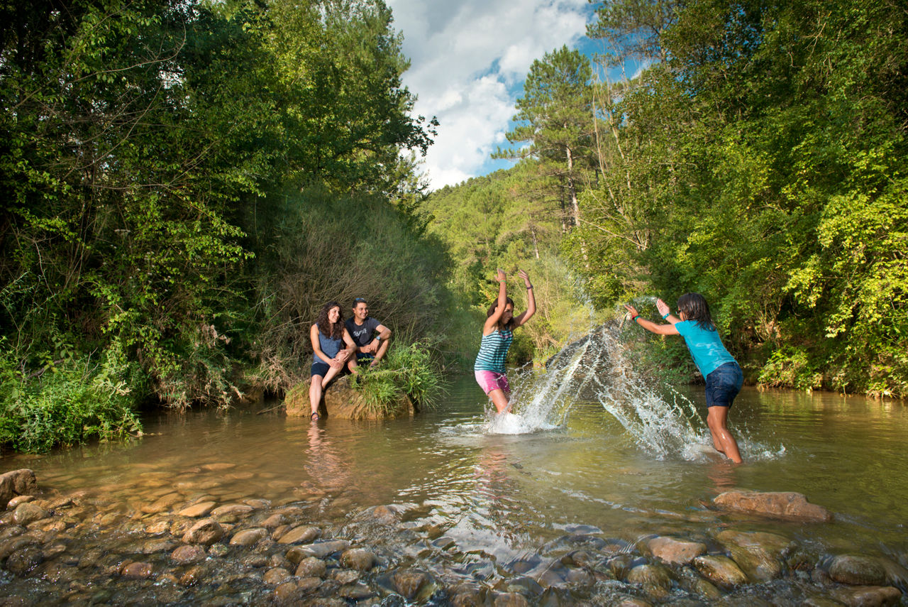 Parella asseguda en una roca i noia i nena jugant amb l'aigua del riu Cardener al seu pas pel municipi de Cardona.