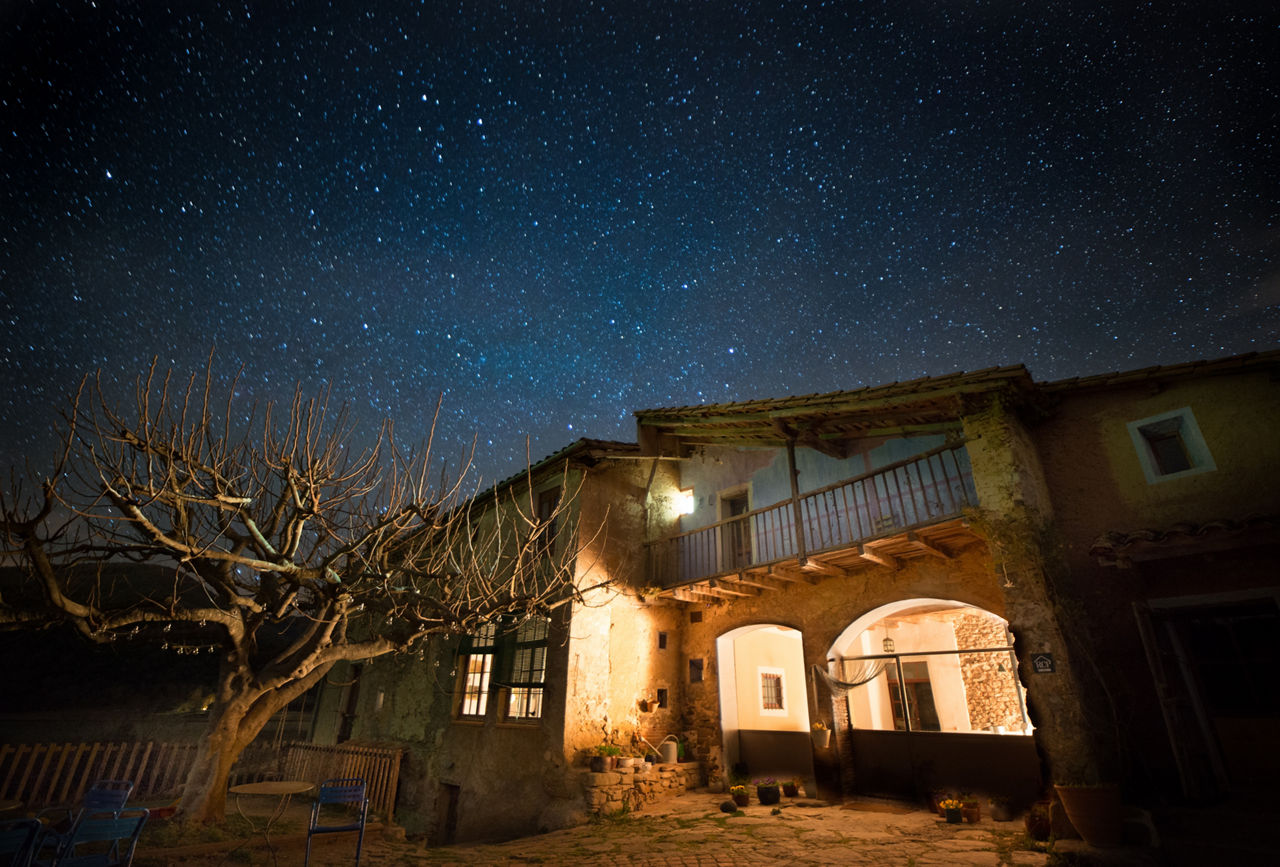 Façana de la Masia Mas Garganta il·luminada a la nit sota un cel estrellat.