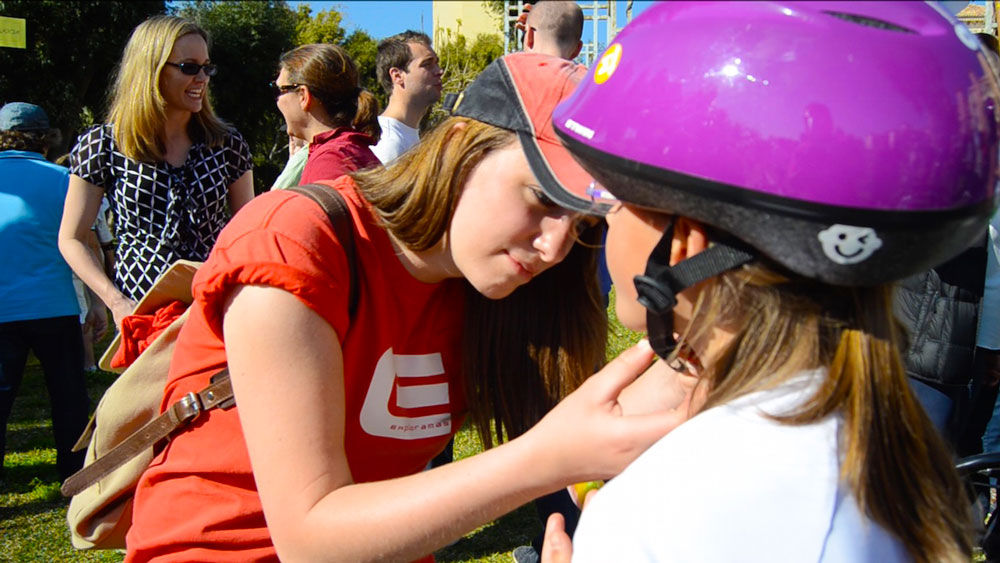 Auxiliar d'Exploramás ajustant la cinta dels casc a una nena durant l'activitat CSR Dream Bikes.