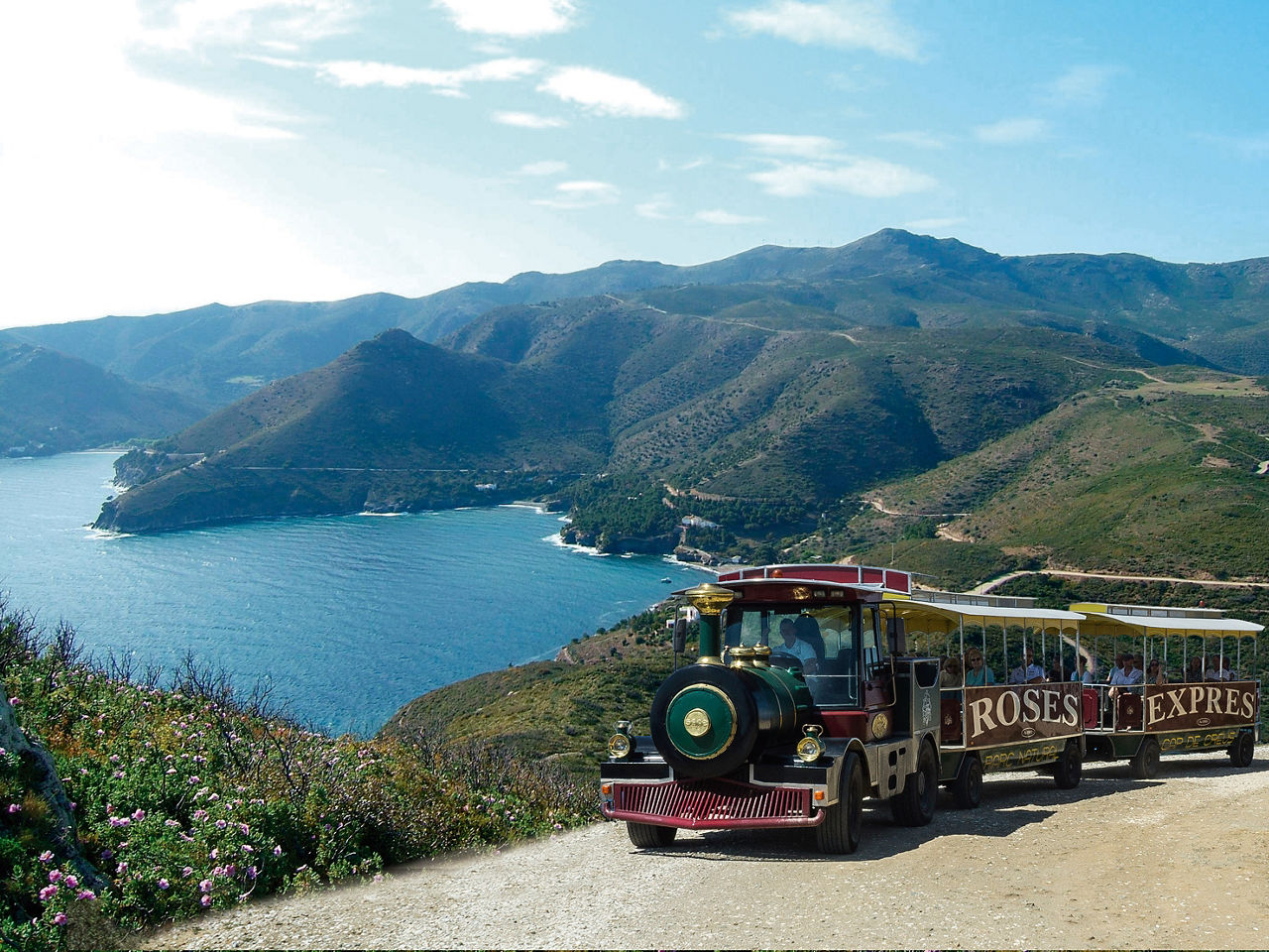 Tren turístic Roses Expres amb una de les cales que recorre durant la ruta Jòncols al darrere.