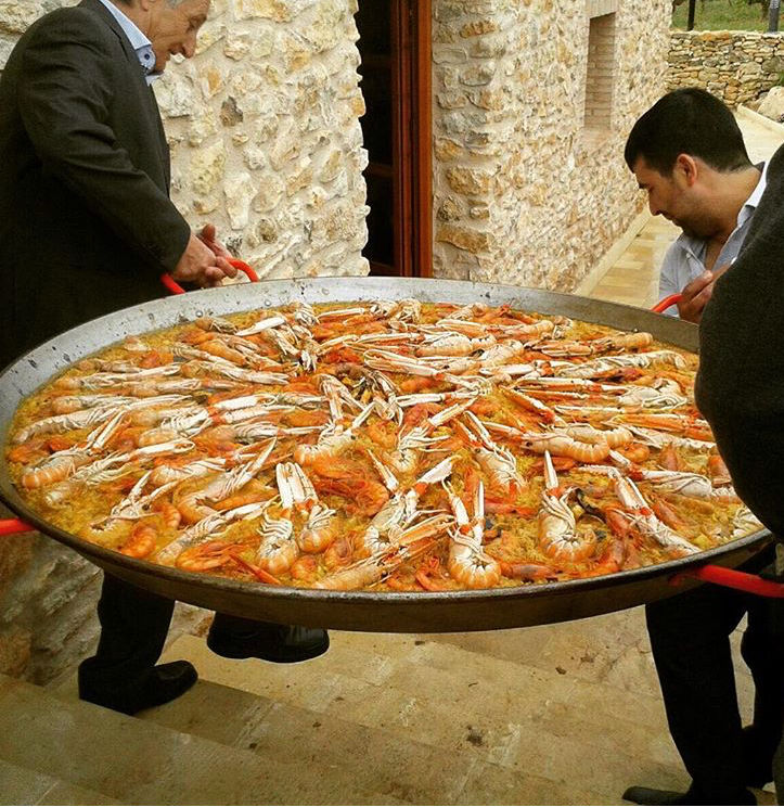 Dos homes traginant una paella.    