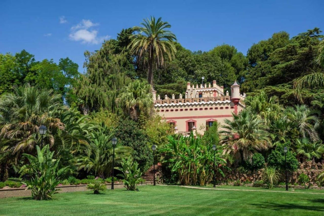 Façana envoltada per palmeres i arbres del jardí de l'hotel de cinc estrelles Villa Retiro, a Xerta.